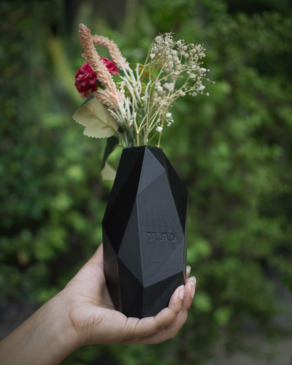 a hand holding a black faceted vase with different types of flowers inside.
